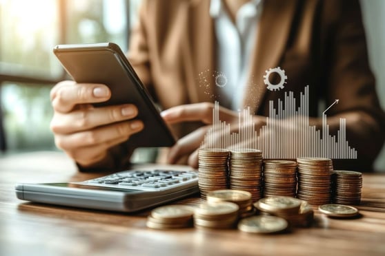 Person sitting at a table with a calculator and piles of coins.