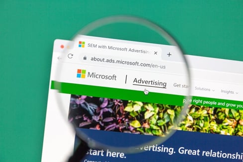 Microsoft Advertising page under a magnifying glass, highlighting its role in b2b advertising platforms for campaigns.